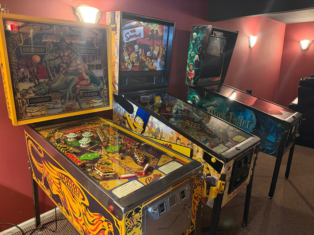 Lost World, The Simpsons Pinball Party, and Harry Potter pinball machines in a red-walled basement game room